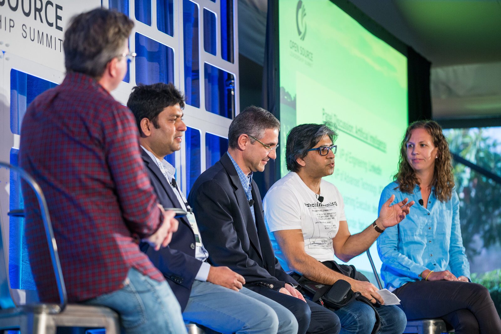 The panel from the side of the stage, all five seated in a row against the summit backdrop, Tarry Singh second from the right in the #machinelearning T-shirt.