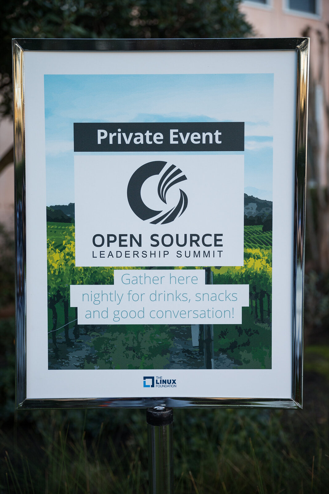 A framed sign standing on the inn's grounds, headed Private Event, carrying the Open Source Leadership Summit mark over a vineyard photograph and the line "Gather here nightly for drinks, snacks and good conversation!"