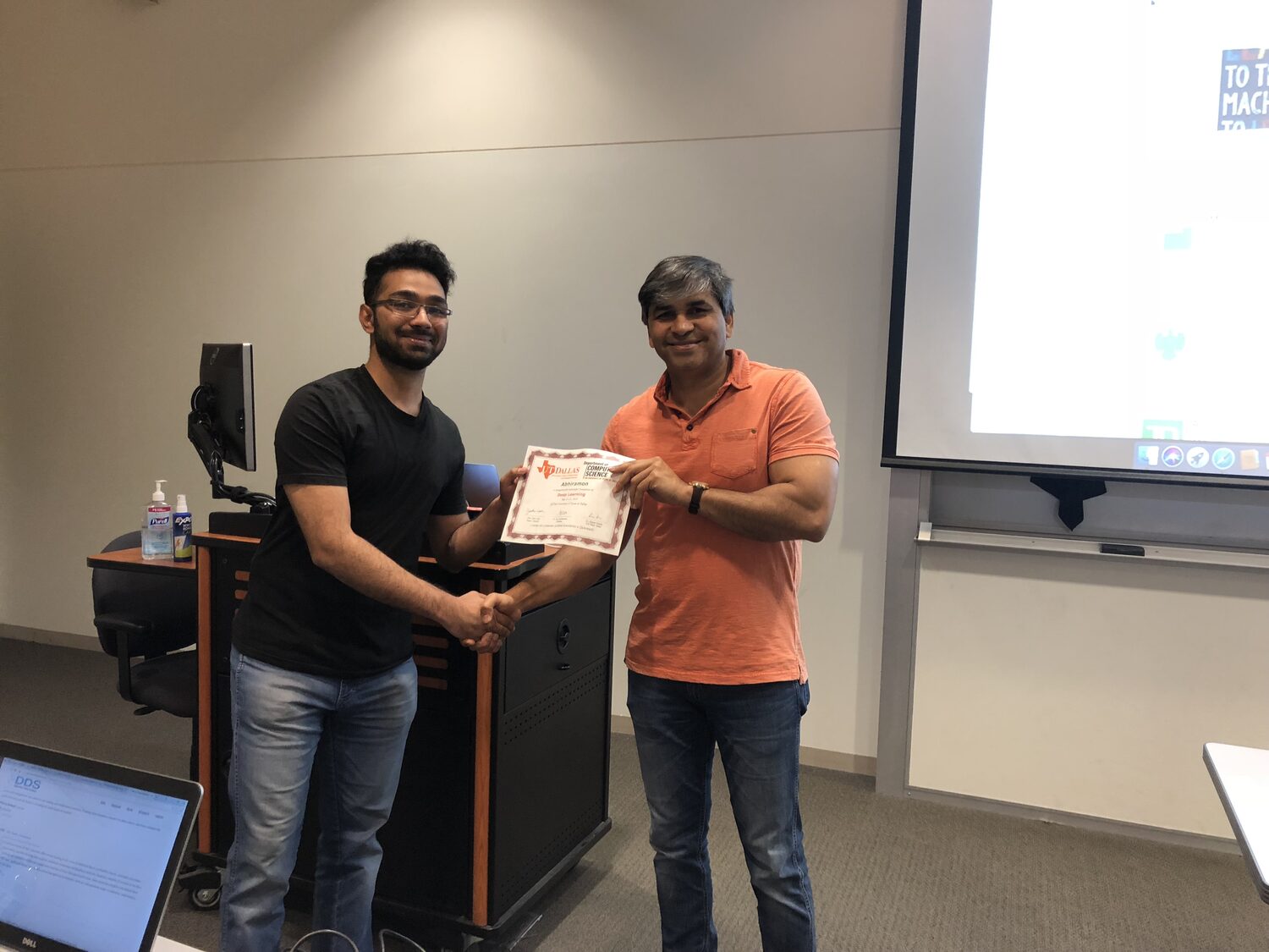 A handshake and certificate handover beside the classroom podium