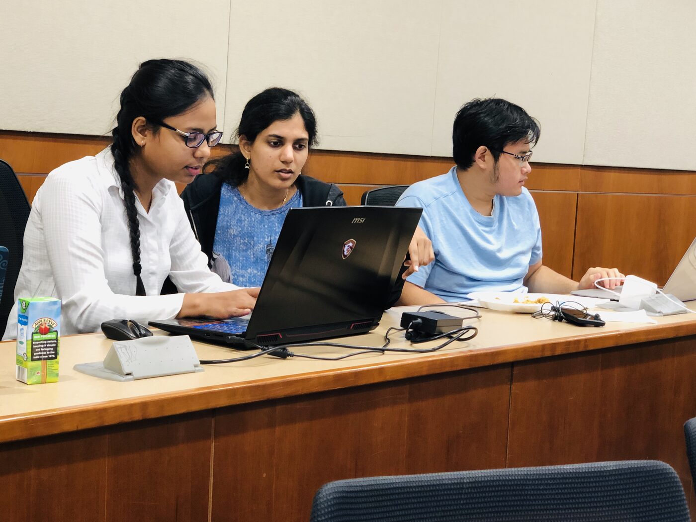 Three participants working through a lab together around a single laptop at a lecture hall desk.
