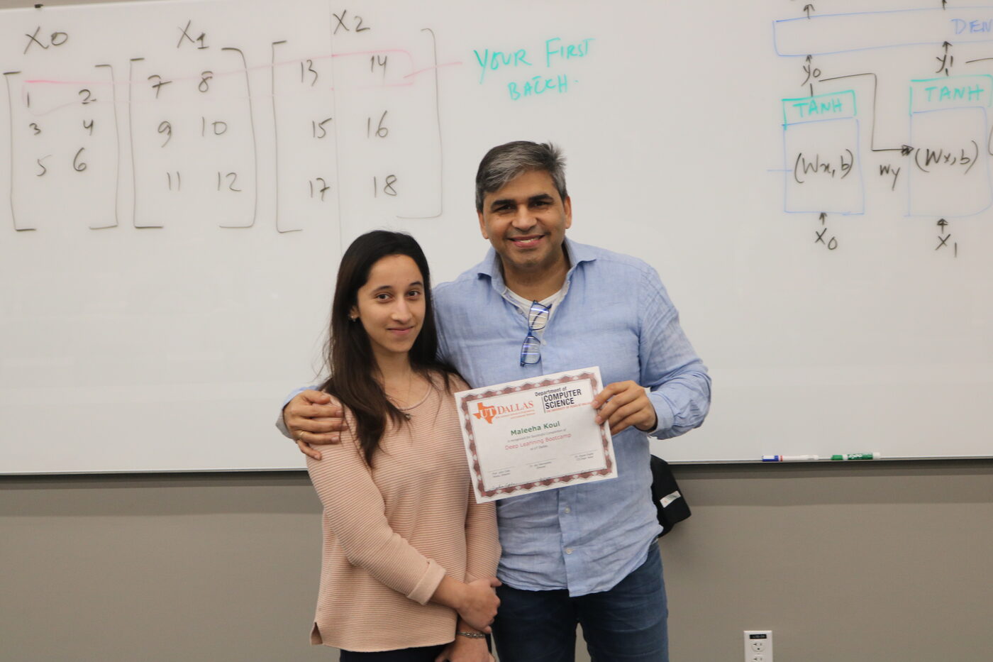 Certificate handover in front of the whiteboard: a participant holds a UT Dallas Department of Computer Science certificate beside Tarry Singh, the lecture diagram and the words your first batch still on the board.