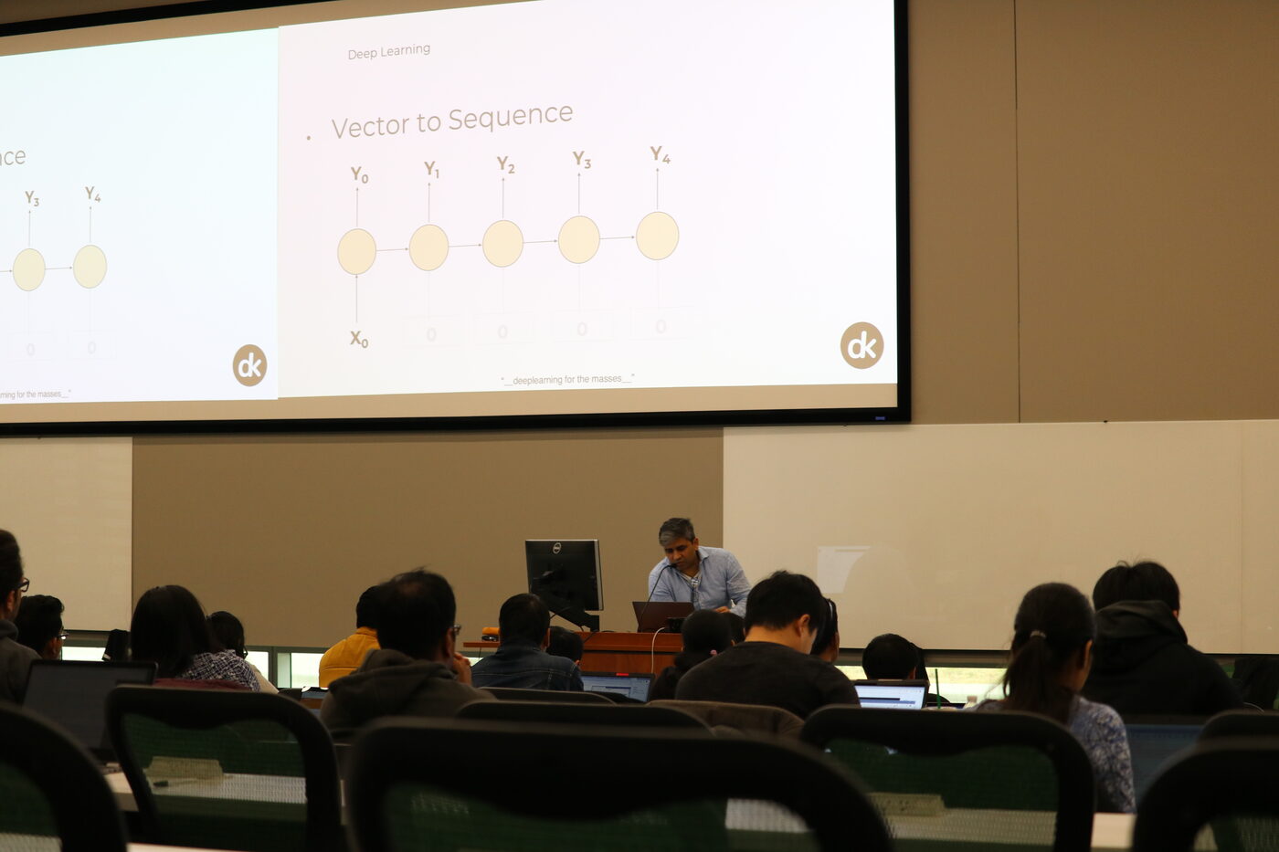 A slide headed Vector to Sequence on the front screen of the hall, the instructor at the podium below it and students in the foreground.