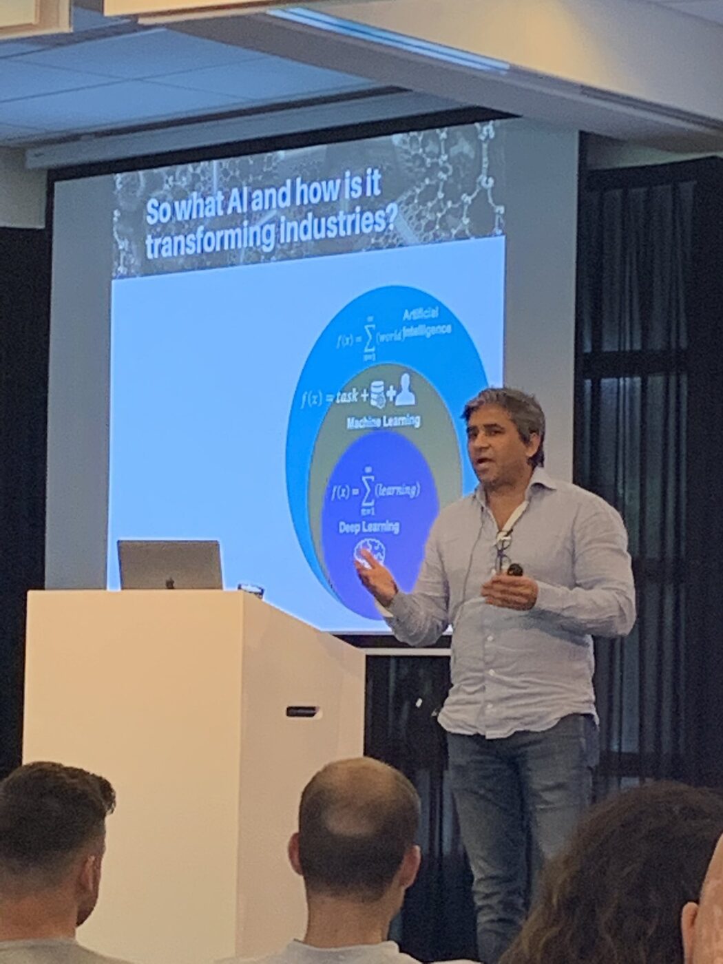 The audience watches a slide asking what AI is and how it is transforming industries, with artificial intelligence, machine learning and deep learning drawn as nested sets.