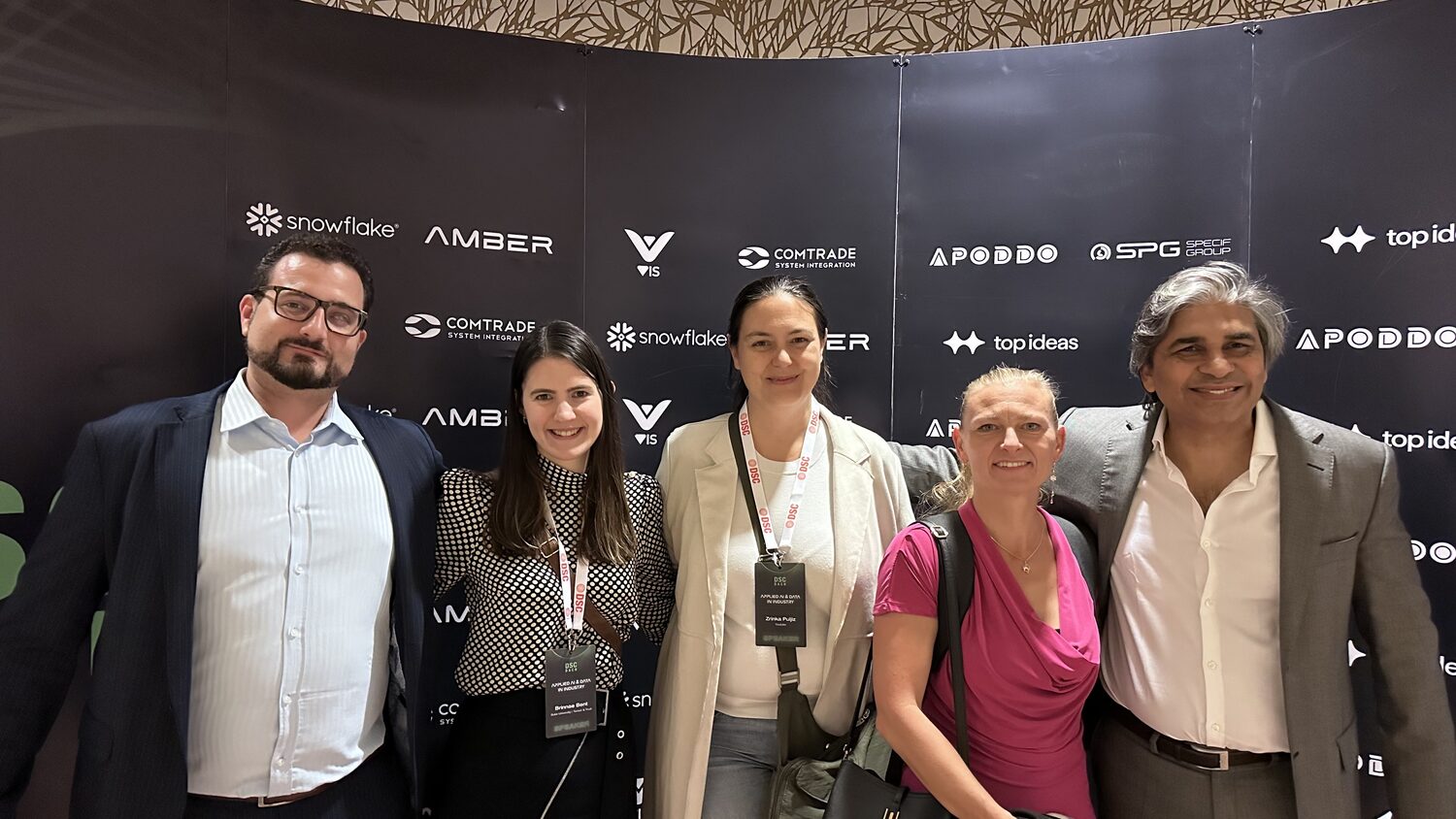 Five delegates standing in front of the DSC DACH sponsor wall, with logos for Snowflake, AMBER, VIS, Comtrade System Integration, APODDO, SPG and top ideas behind them