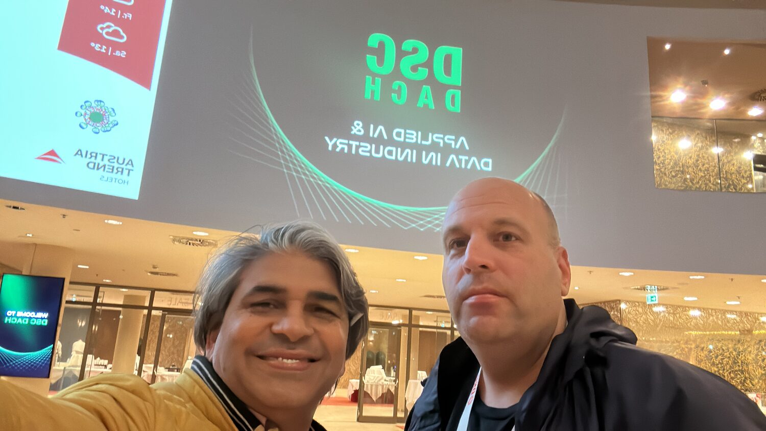 Two attendees in the hotel lobby in front of the DSC DACH title screen reading Applied AI and Data in Industry