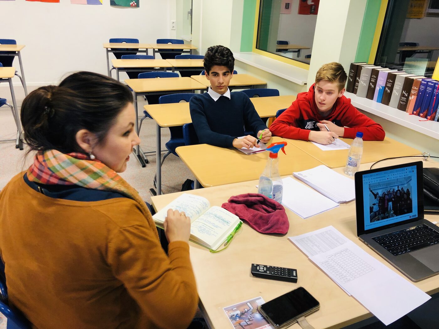 Two pupils at pushed-together desks with notebooks open and pens in hand, following the session; a laptop on the table shows the deepkapha.ai website.